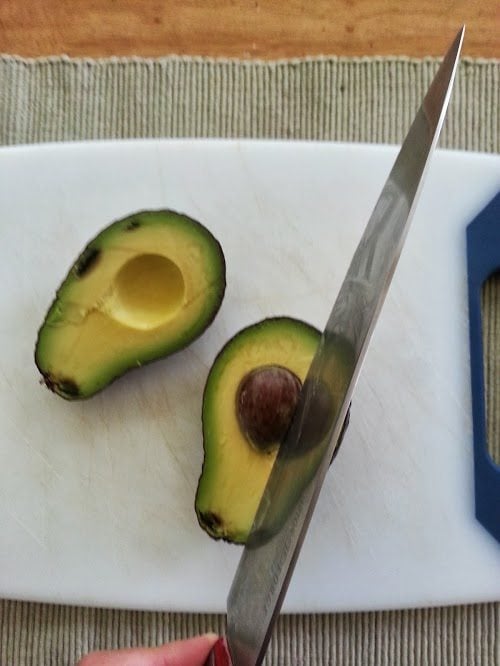 An avocado cut in half and a knife in the center of the avocado seed.