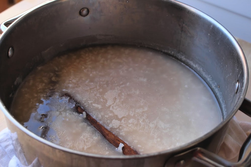 Cooked rice in murky water with cinnamon sticks floating inside a stock pot. 
