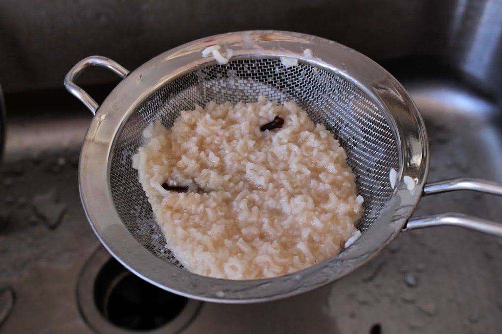 Draining rice and cloves through a strainer over the sink. 