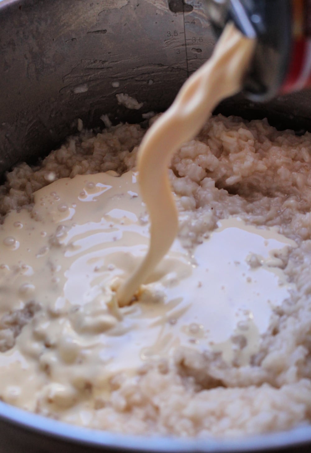 Evaporated milk pouring into the stock pot with cooked rice. 