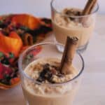 Pumpkin Arroz con Leche served in a glass cup topped with raisins and a cinnamon stick to the side.