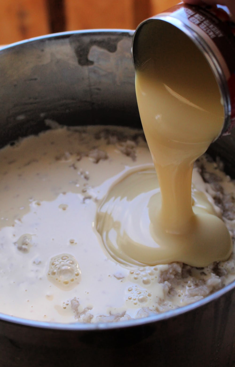 Sweetened Condensed Milk pouring into the stock pot with rice and evaporated milk. 