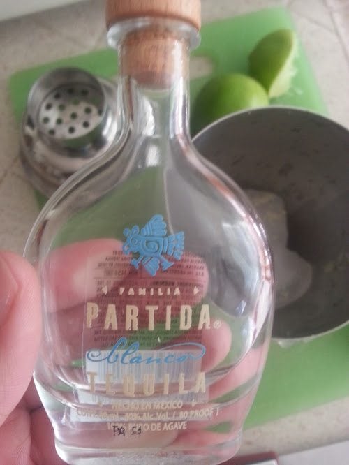 Holding Partida Blanco Tequila bottle and some lemons and ice