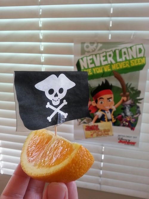 Hand holding an orange wedge topped with a pirate flag.