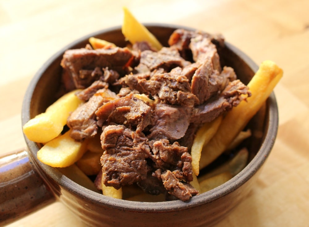 Fries in a brown bowl topped with carne asada.