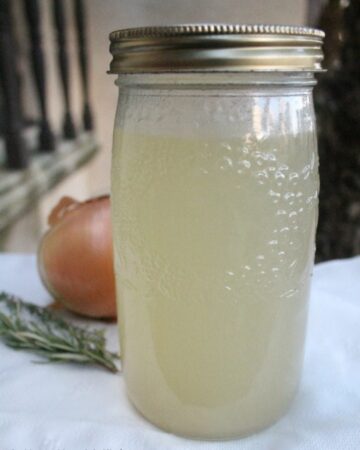 A jar of chicken stock next to onion and rosemary.