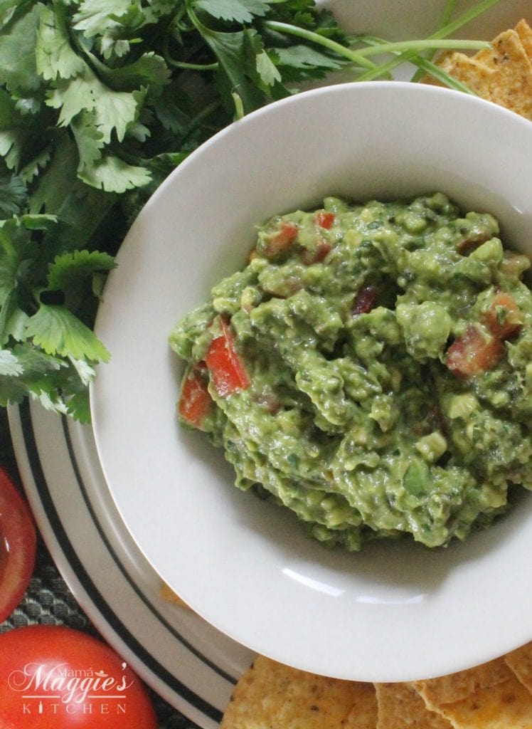 Quick and Easy Guacamole served on a bowl decorated with cilantro and tomatoes