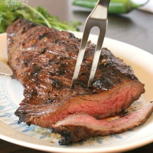 A fork inserted in the center of a grilled tri tip with a slice cut off from the meat.