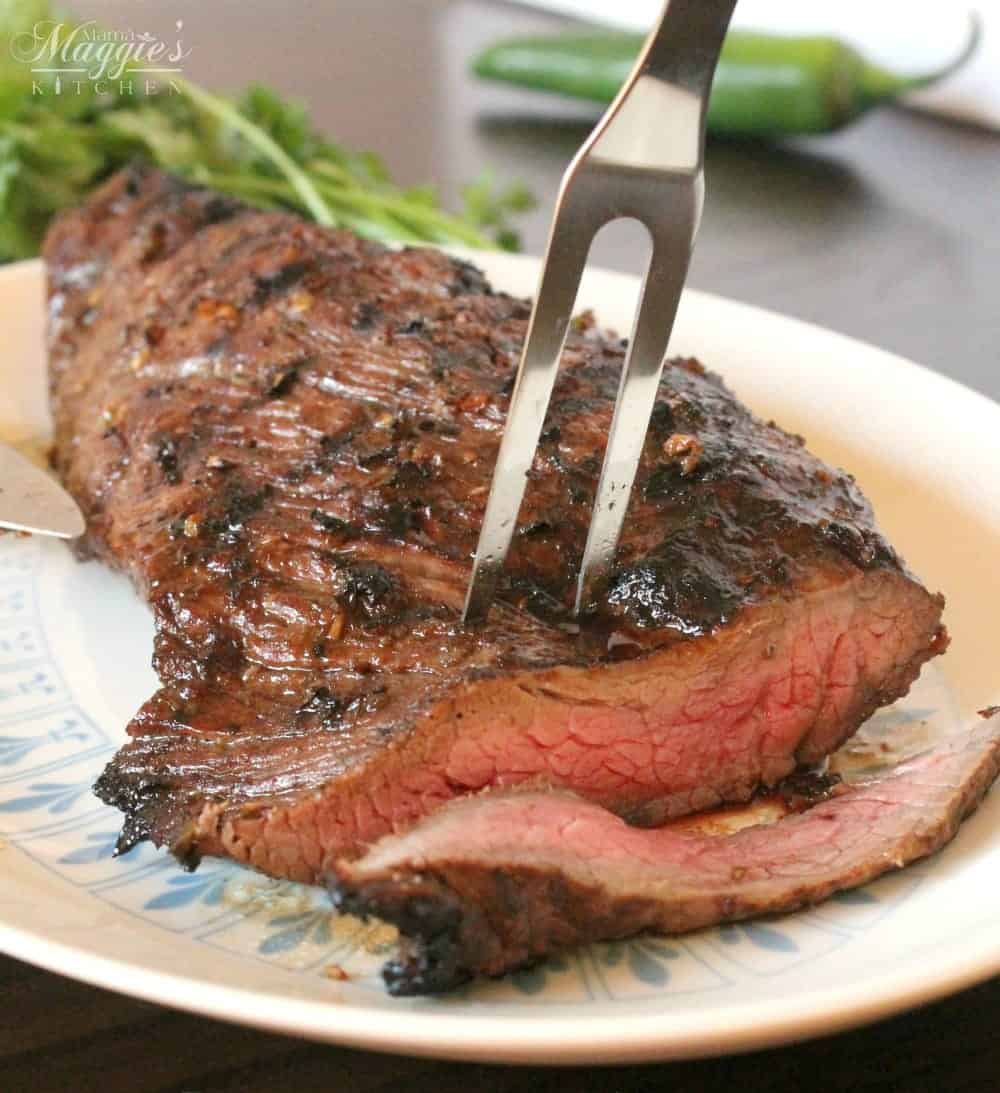 A fork inserted in the center of a grilled tri tip with a slice cut off from the meat.