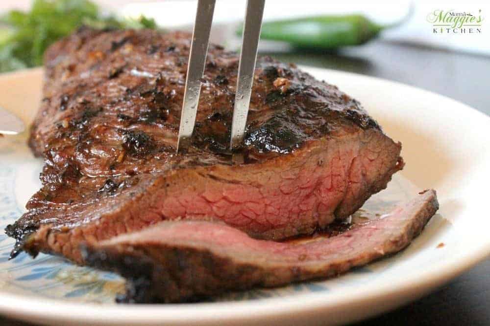 A fork inserted into the center of a grilled tri tip and a slice of meat cut off.