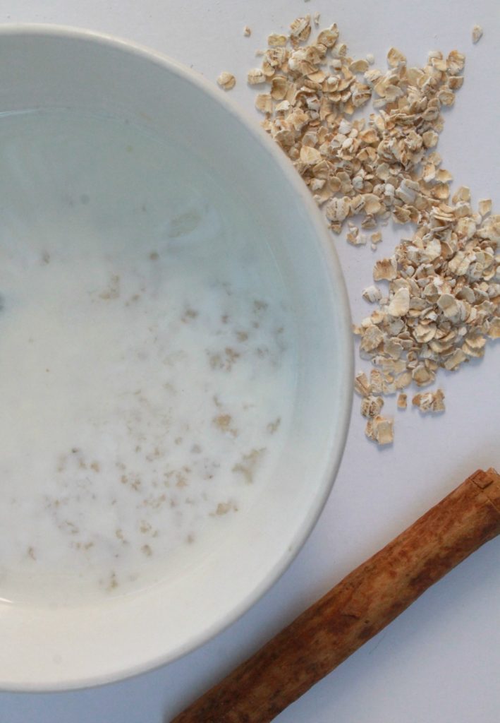A white bowl of avena next to dried oatmeal and a cinnamon stick.