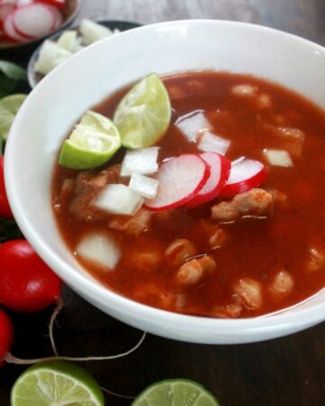 Pozole Rojo in a white bowl and topped with lime and radish slices.