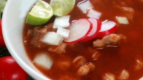Pozole Rojo in a white bowl and topped with lime and radish slices.
