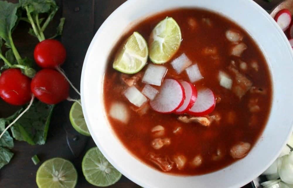 Pozole Rojo in a white bowl topped with radishes and lime.
