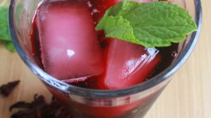 Agua de Jamaica in a glass with ice and garnished with mint leaves.
