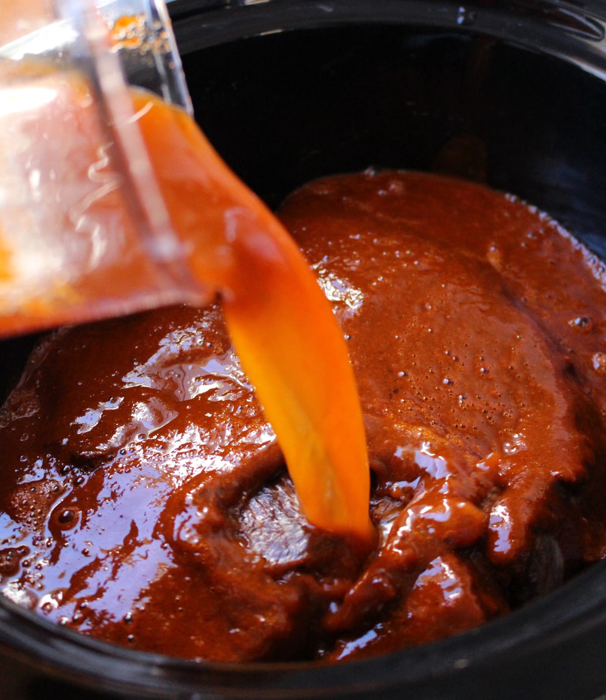Chile sauce pouring into the slow cooker over the beef.