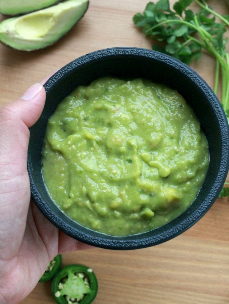 A hand holding a bowl of salsa de aguacate.