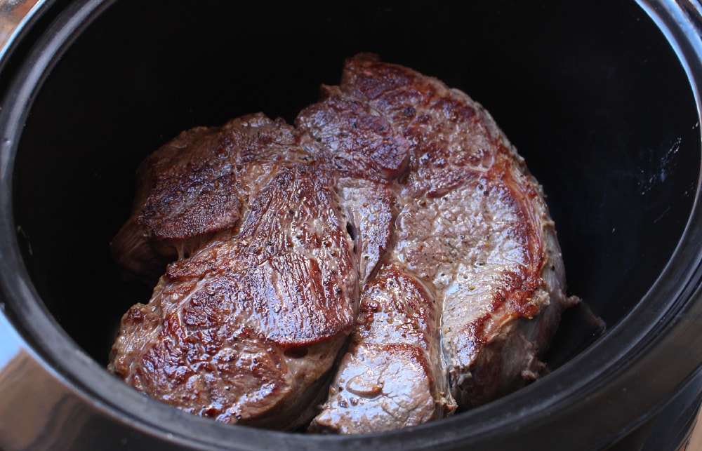 Seared beef in a black slow cooker.
