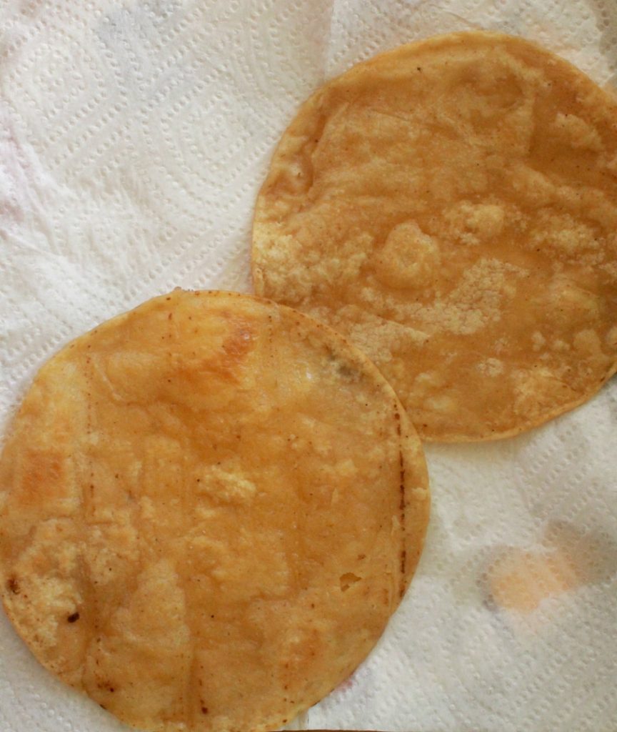 Two tortillas draining excess oil on paper towels.
