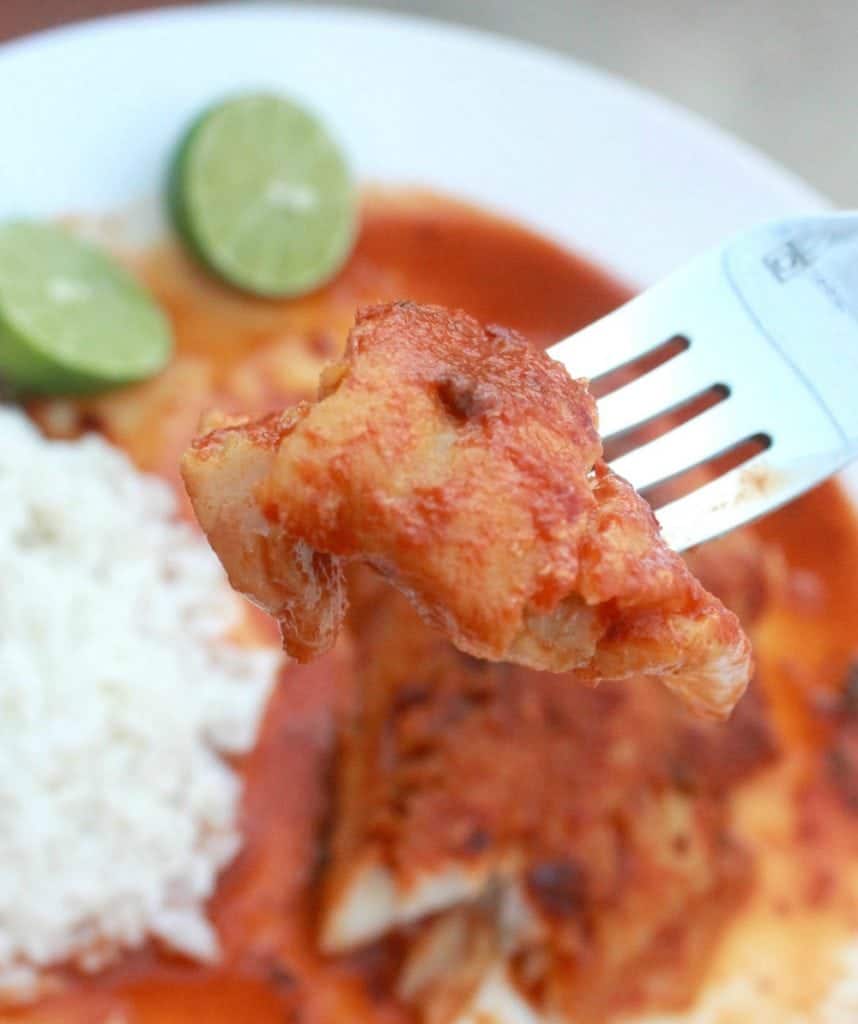 A fork holding a piece of pescado en salsa over a plate. 