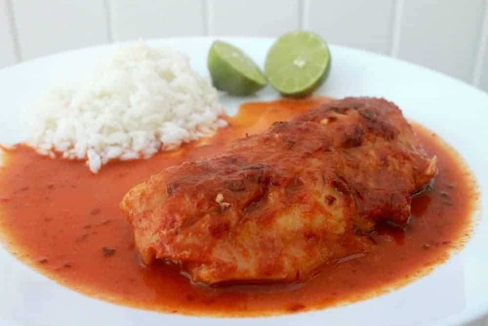 Pescado en salsa served on a whit plate next to rice and lime wedges.