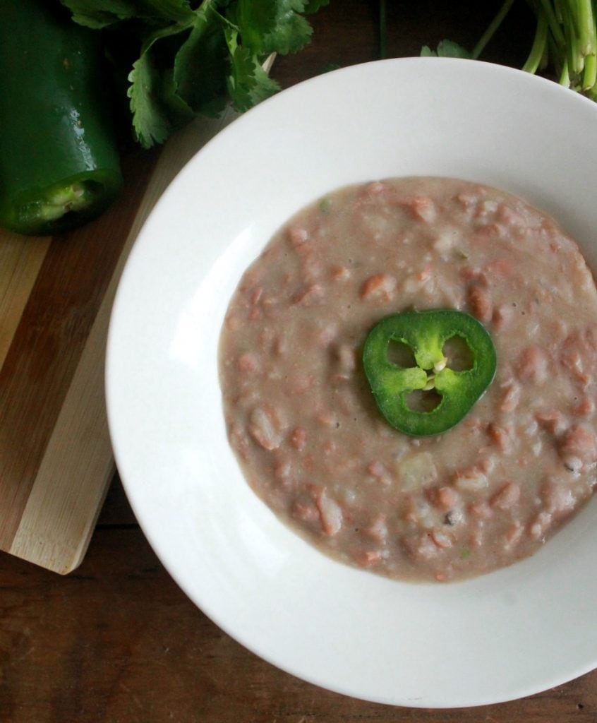 Refried Beans, or Frijoles Refritos, in a white bowl topped with a jalapeno slice.