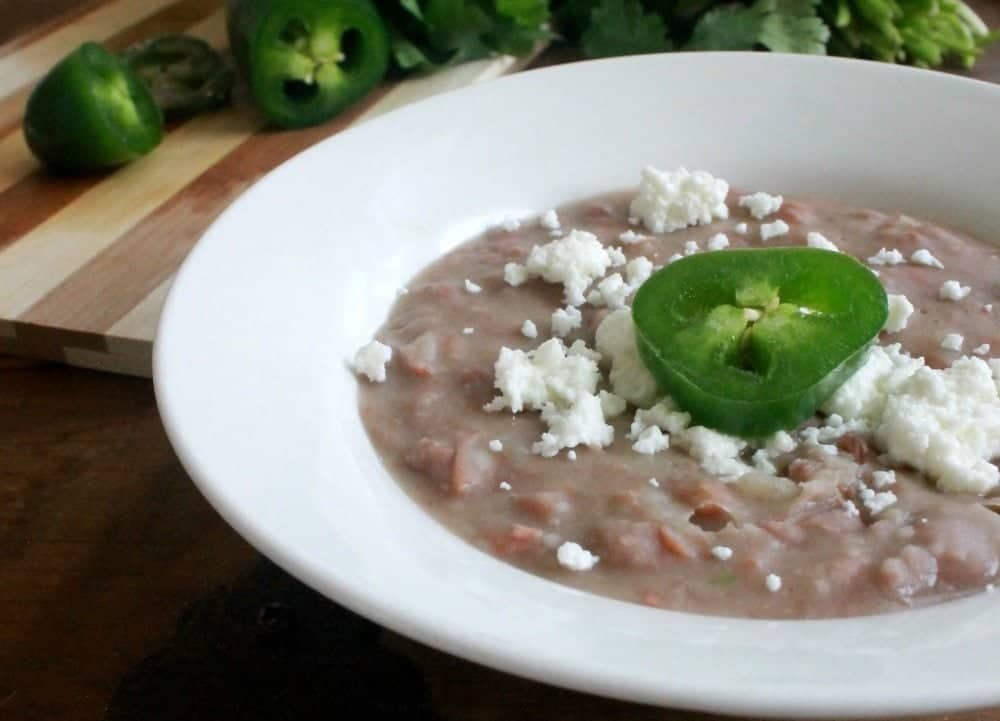 Refried Beans, or Frijoles Refritos, in a white bowl topped with a slice of jalapeno.