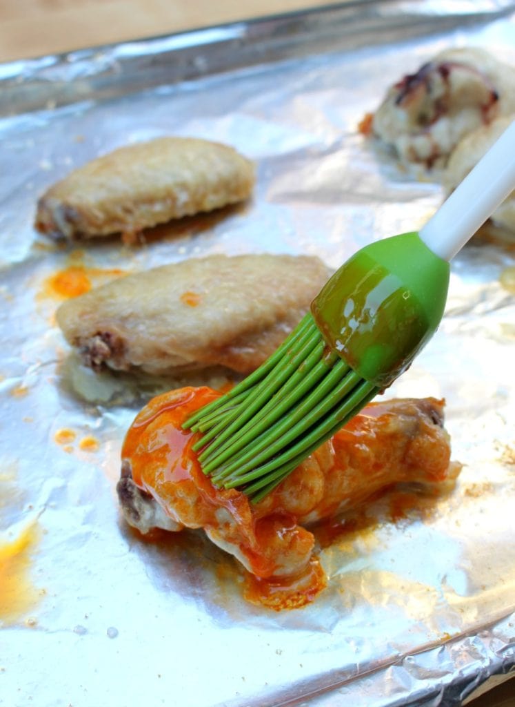 Green brush covering chicken wings with Buffalo Chicken Wing sauce.