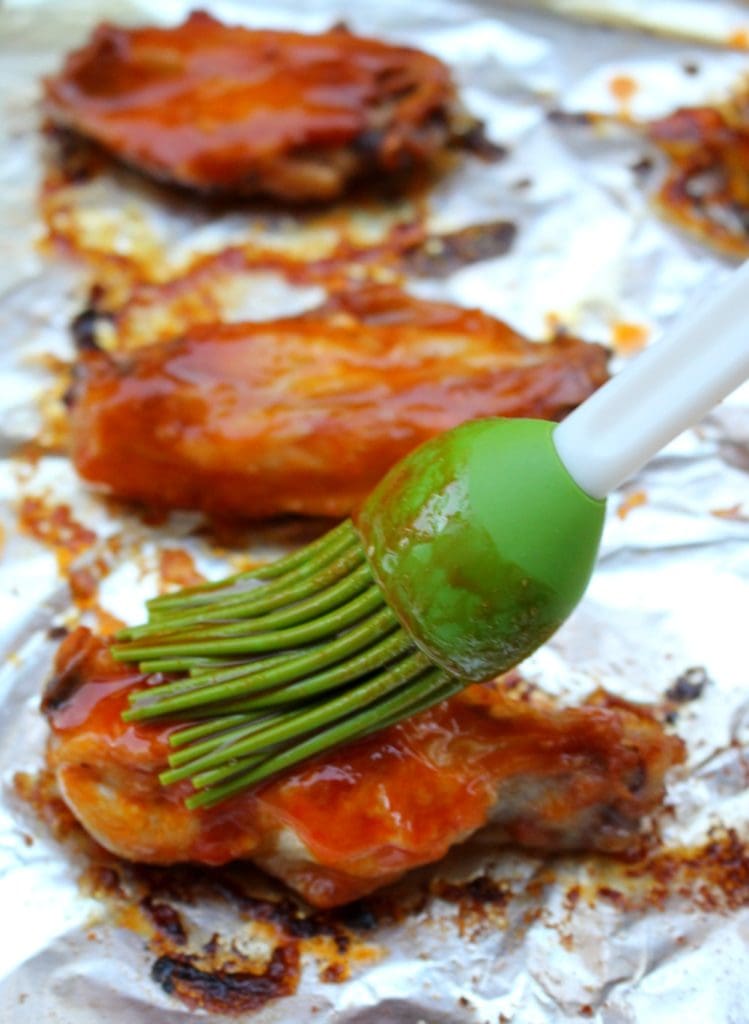 Green brush brushing sauce on chicken wings. 