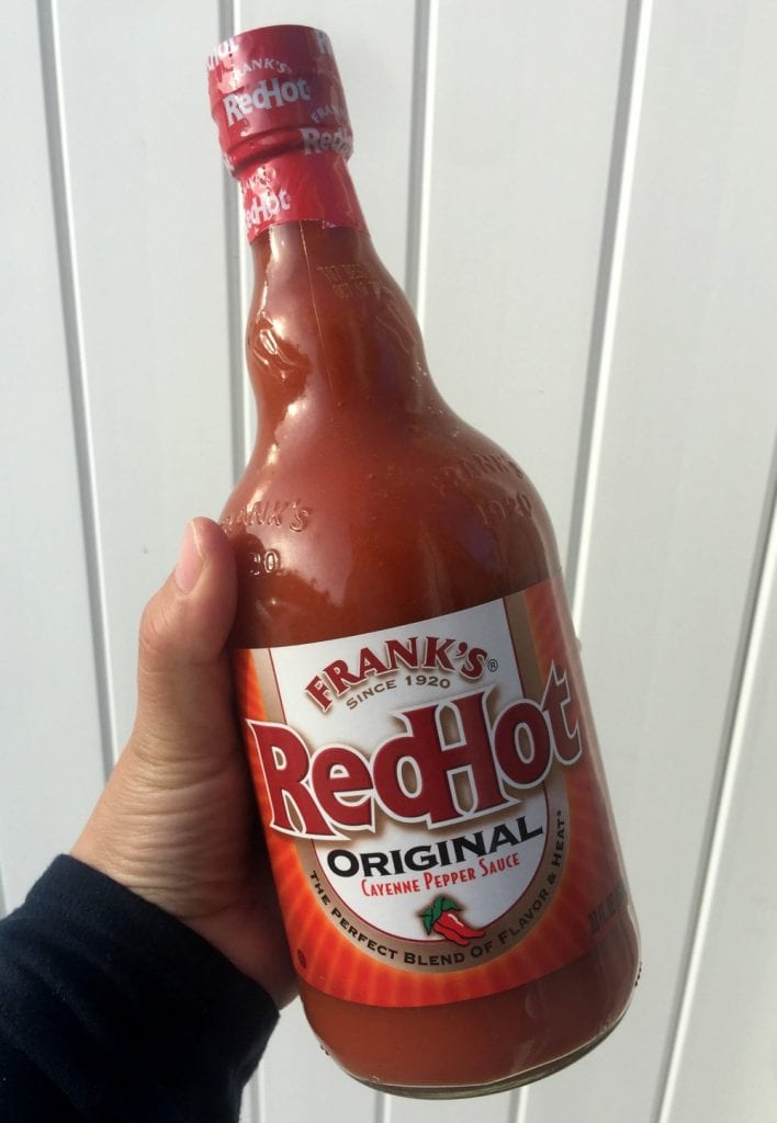 Hand holding a bottle of Frank's Red Hot sauce. 