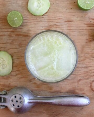 Cucumber Lime Agua Fresca served in a glass with ice and surrounded by slices of cucumber and lime wedges.