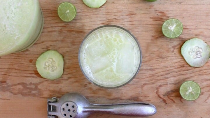 Cucumber Lime Agua Fresca served in a glass with ice and surrounded by slices of cucumber and lime wedges.
