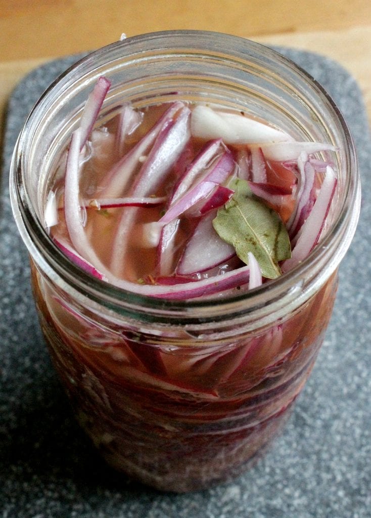 Sliced red onions in a jar with bay leaves and submerged in a vinegar mixture.
