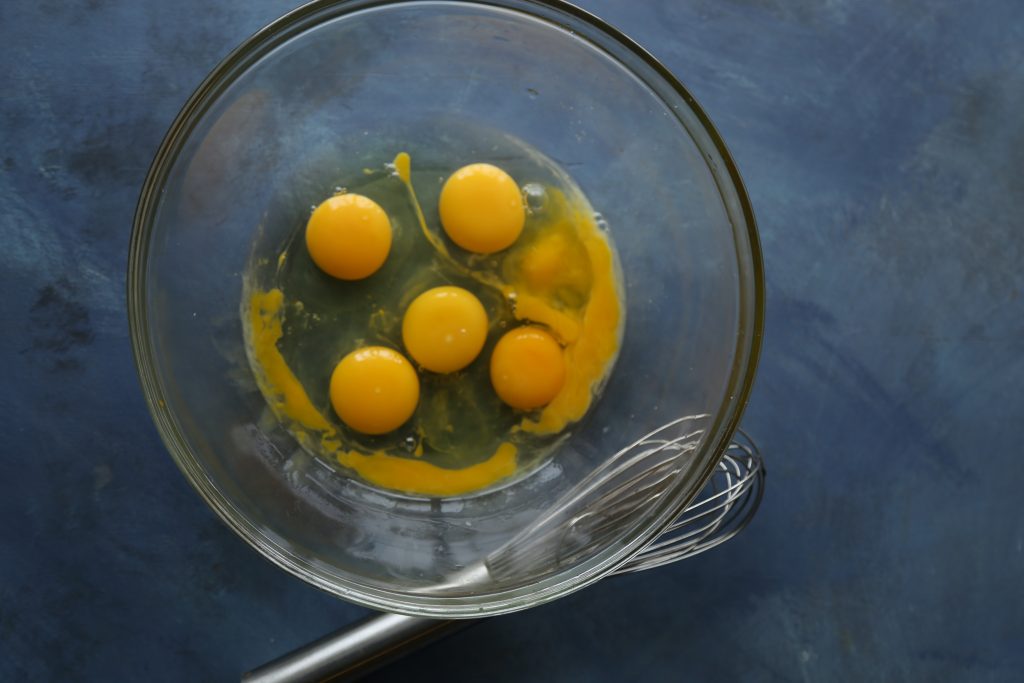 A bowl with raw eggs next to a whisk.