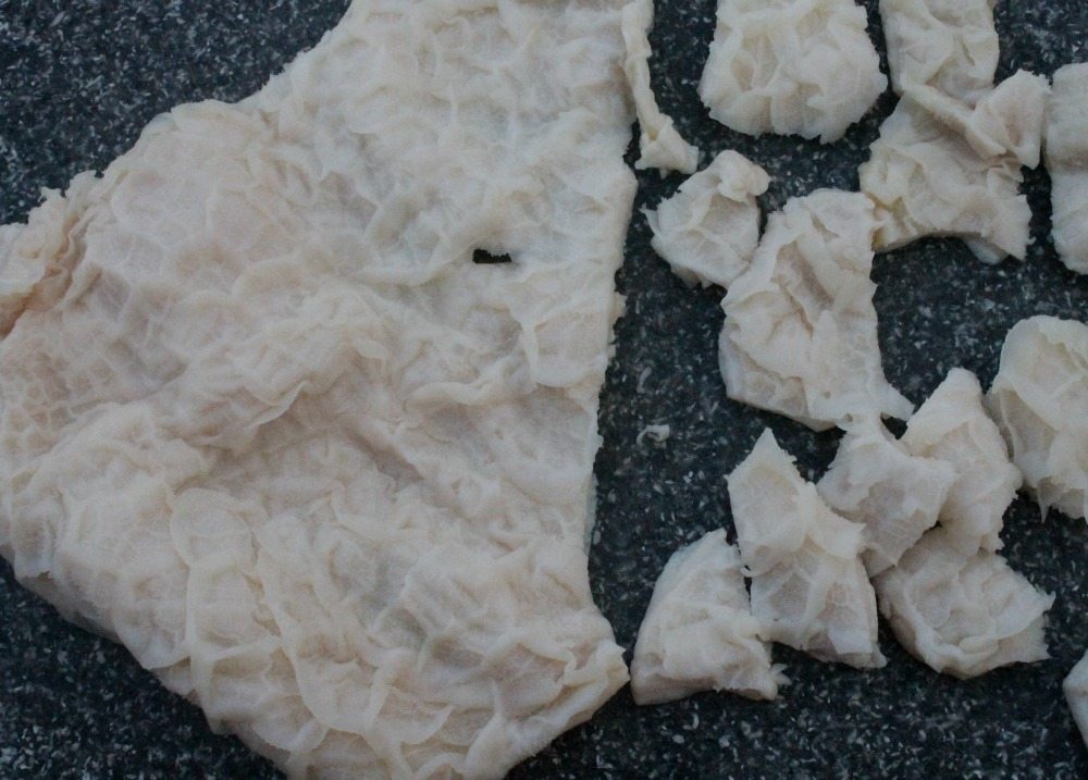 Honeycomb tripe partly chopped up on a cutting board.