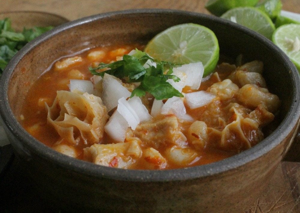 Menudo, or Pancita, in a brown bowl and topped with onion and cilantro.