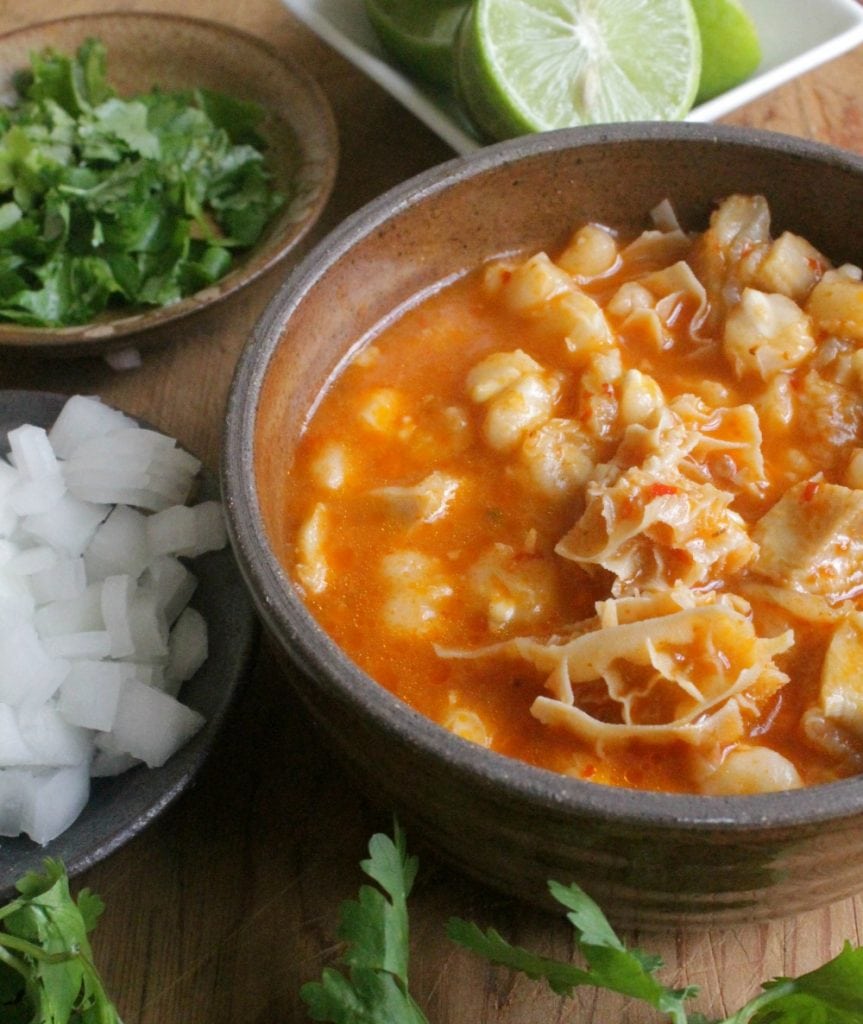 Menudo, or Pancita, served in a brown bowl and surrounded by the toppings.