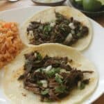 Two beef tacos topped with onions and cilantro served on a white plate.