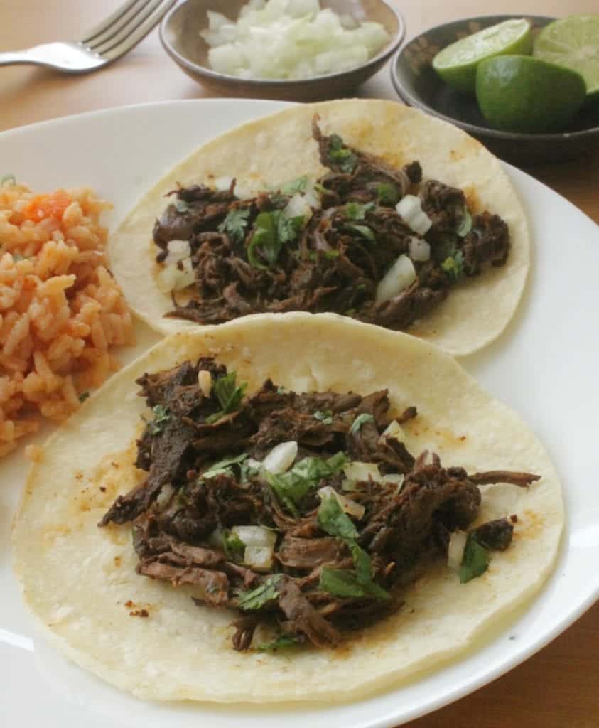 Two beef tacos topped with onions and cilantro served on a white plate. 