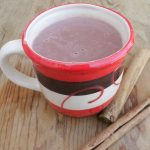 Atole de Chocolate in a decorative red and brown cup next to two cinnamon sticks.