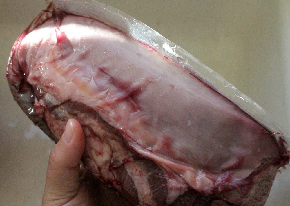Hand holding a package of beef tongue still in the wrapper.