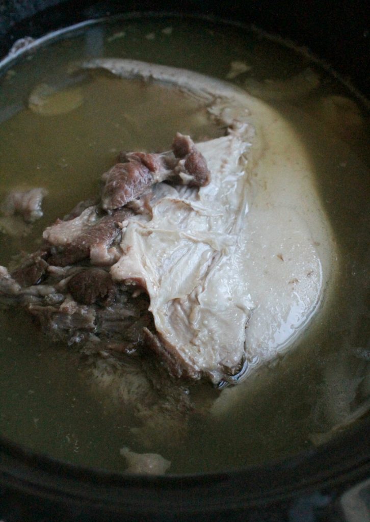 Cooked cow tongue in the slow cooker swimming in the cooking juices.