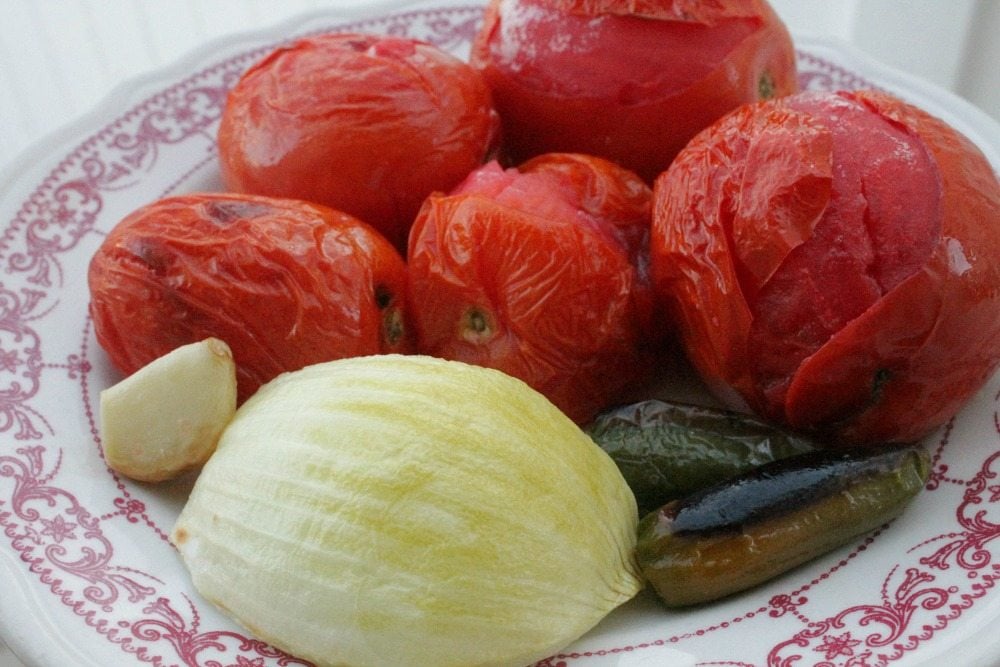 Roasted tomatoes, garlic, onion, and jalapeno on a white plate.