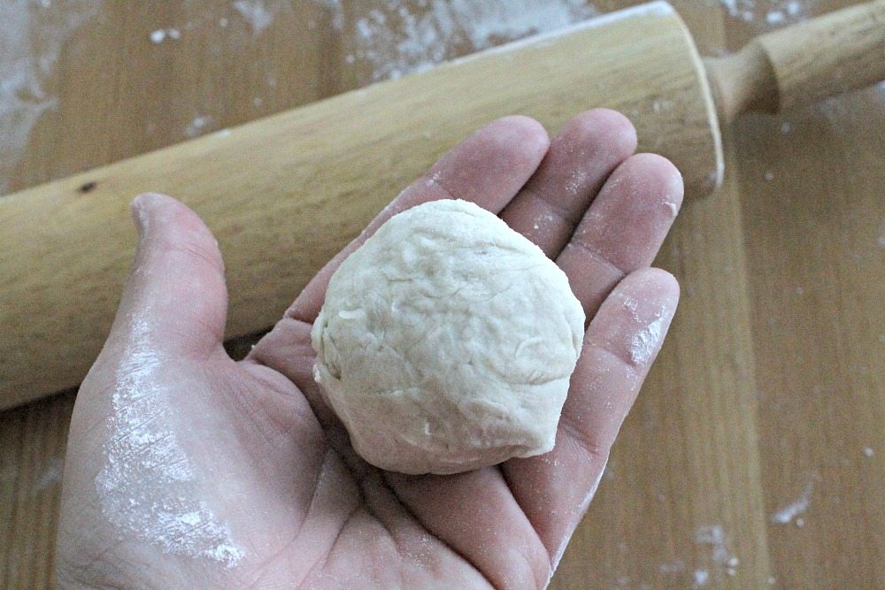 Ball of Dough in Hand with Rolling Pin in the Background