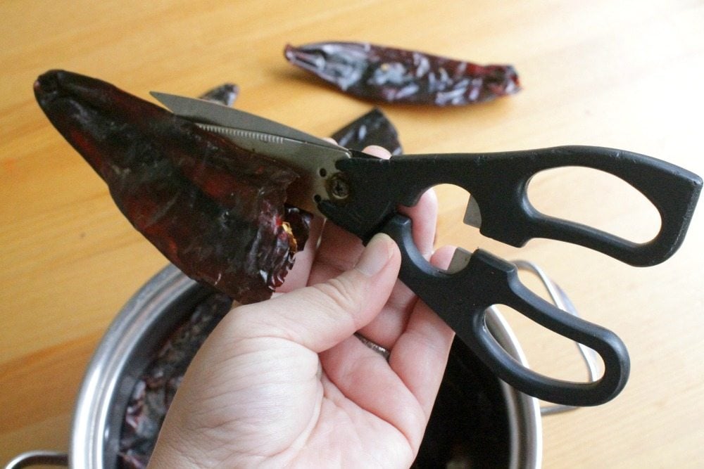 Hand holding scissors and cutting into guajillo chile