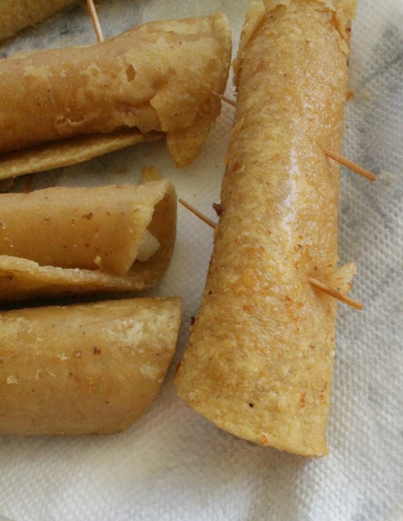 Fried taquitos with toothpicks laying on a paper towel