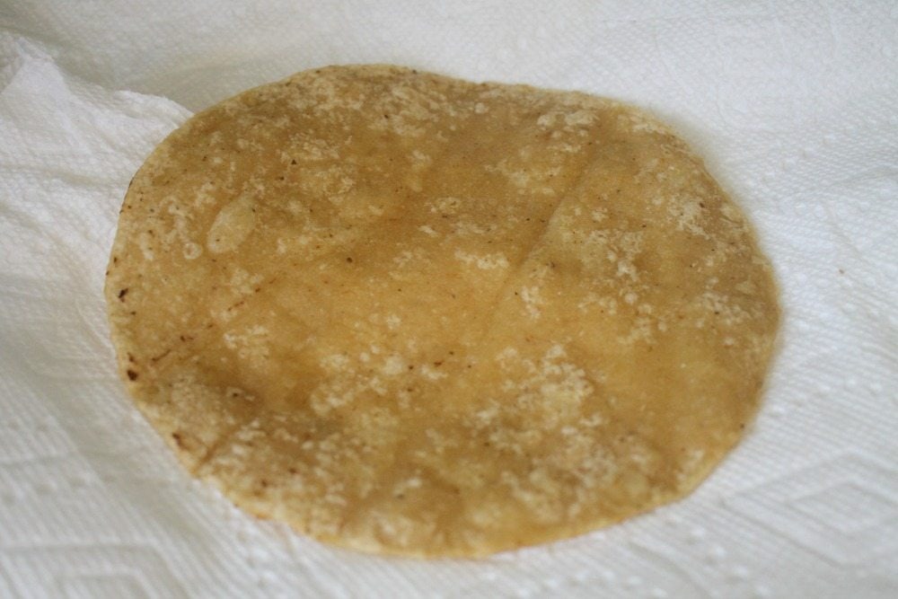 Fried tortilla draining excess fat on a paper towel