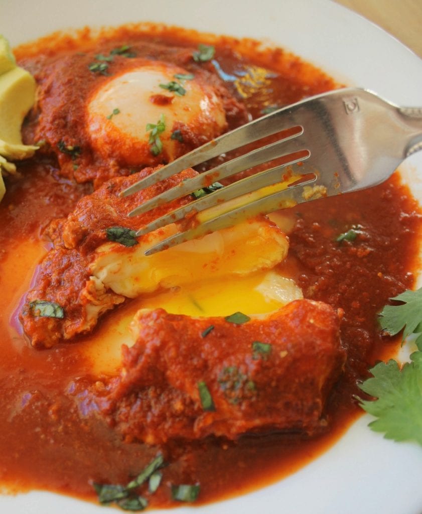 A fork cutting down into a drowned egg in guajillo sauce.