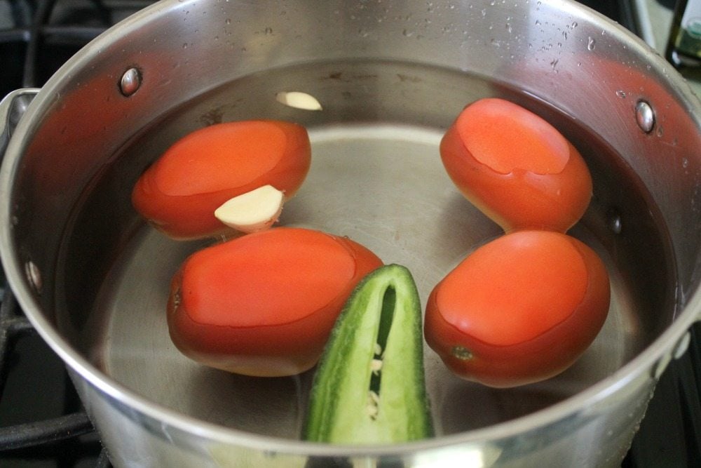 Red Roma tomatoes, jalapeno, and garlic in a pot of water