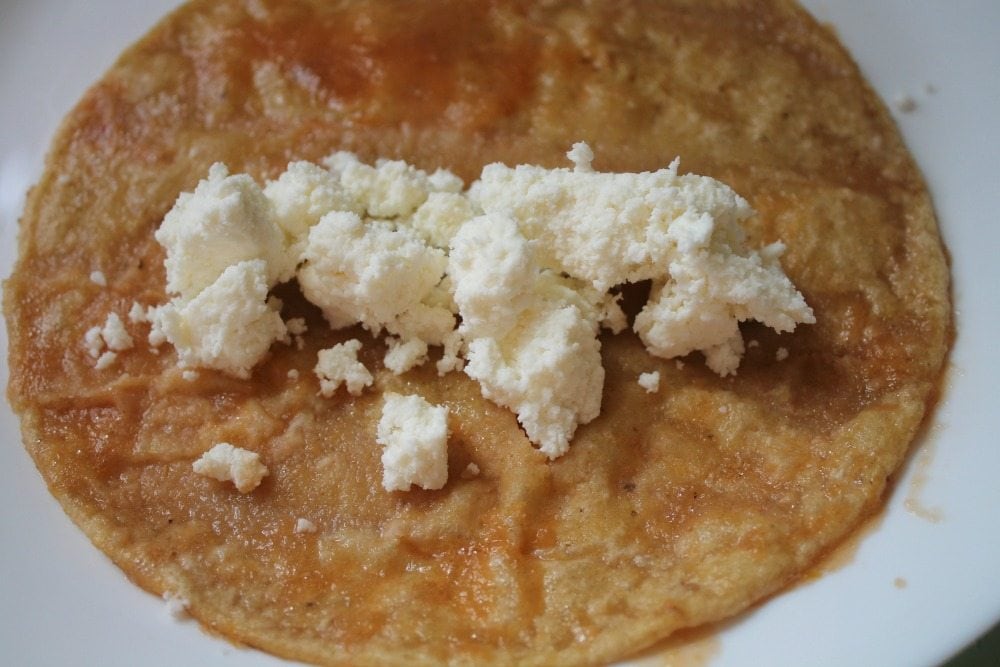 Adding crumbled queso fresco to a fried tortilla dipped in Mexican red salsa